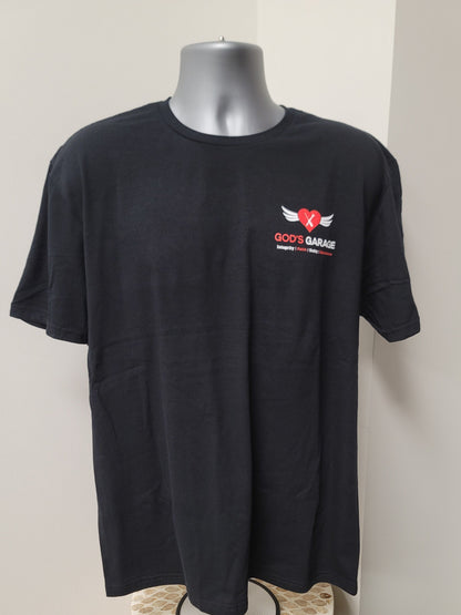 A black short-sleeve t-shirt displayed on a gray mannequin torso against a plain light beige wall. The shirt features a small graphic on the left chest with a red heart, white wings, and the text 'GOD'S GARAGE' in white and red.